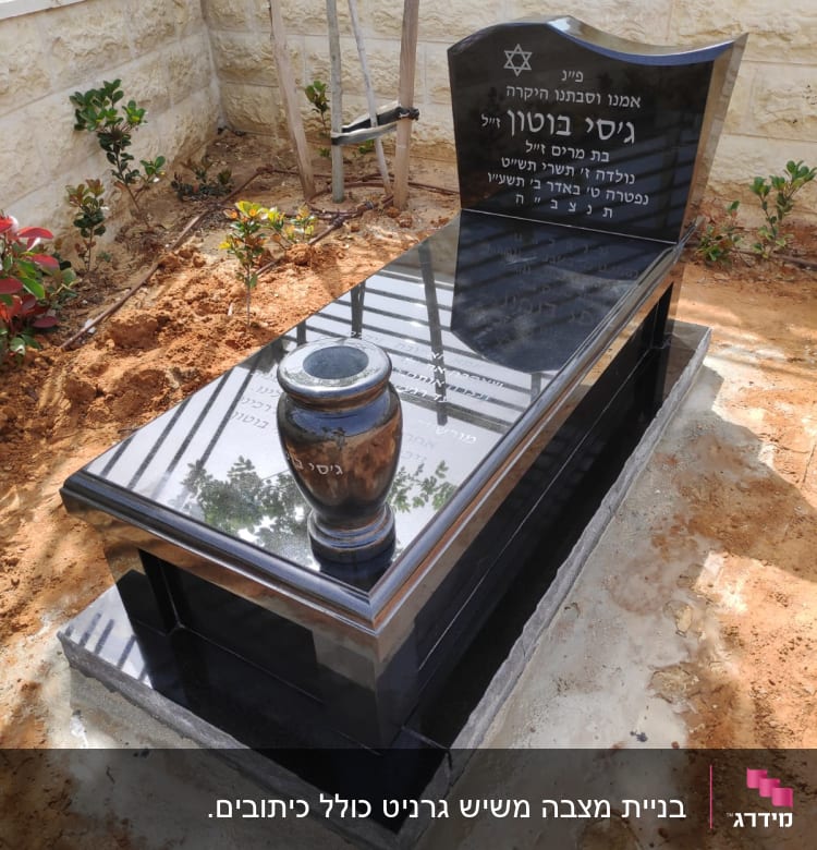 מצבה שחורה עם כיתוב בעברית ואגרטל עליון